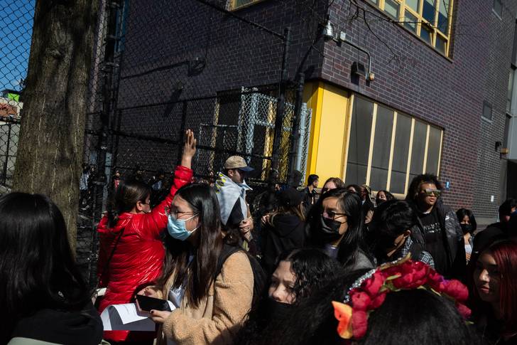 A crowd of students leave Sunset Park High school, with the school and a fence in the background